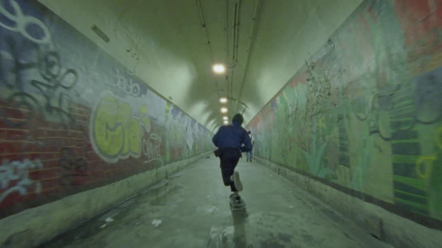 A person skateboards through a spray painted tunnel