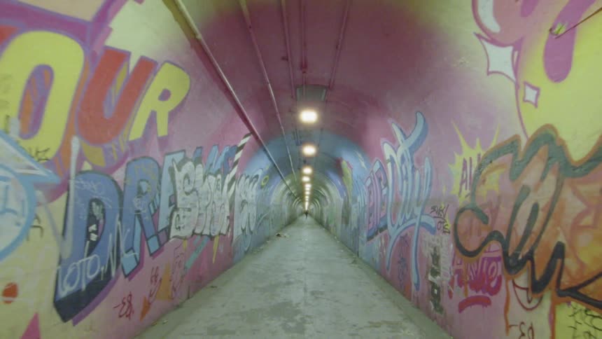 A tunnel with generous overhead lighting is covered floor to ceiling in colorful graffiti made up for words and pictures