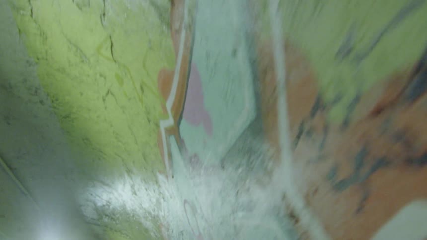 The interior of a concrete tunnel is painted with street art and is observed at pace