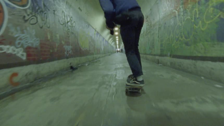 A skateboarder rides through a tunnel with graffiti