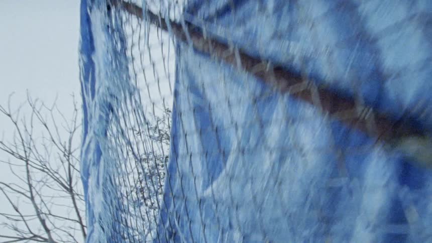 A tattered blue tarp hangs from a chain linked fence