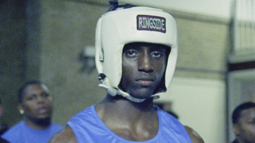 A young fighter prepares to enter the ring as a number of spectators gather to watch