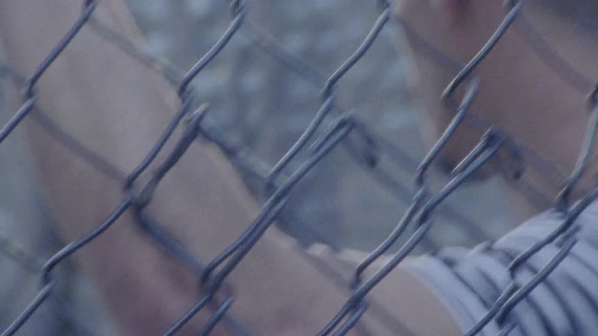 A man holds onto a chain linked fence and talks
