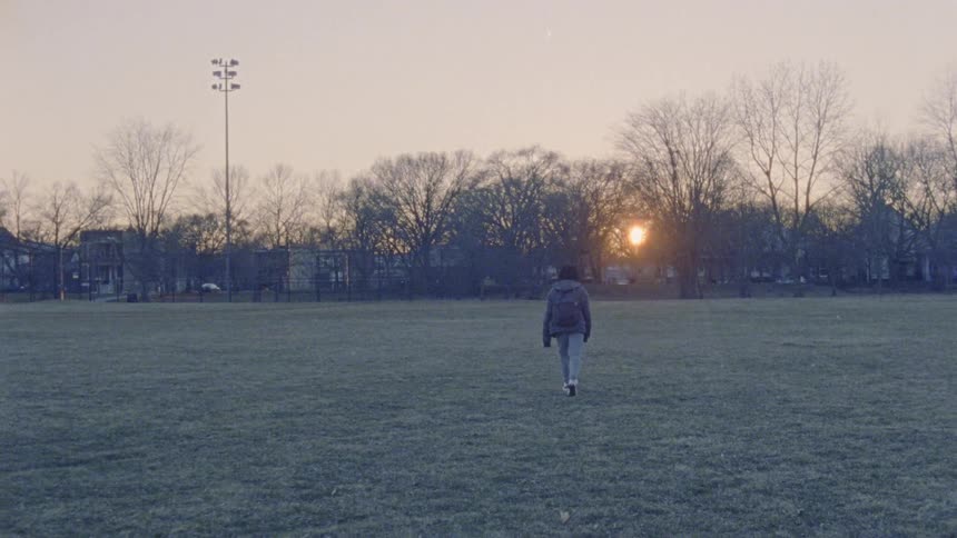 Person walks across a large field at sunset