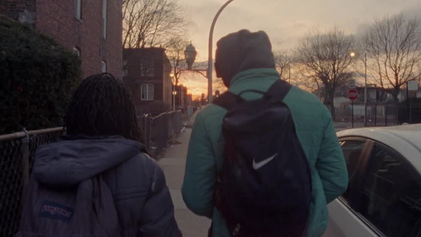 Two school children wearing backpacks walk down the sidewalk