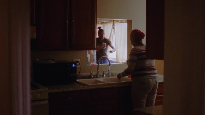 Woman washing dishes in the sink while a man punches the air