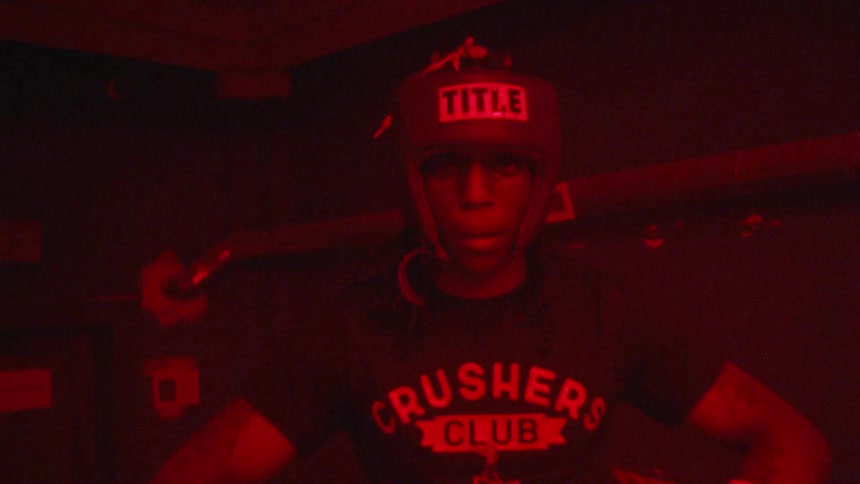 Man wearing boxing gloves and protective headgear stands in the corner of a boxing ring