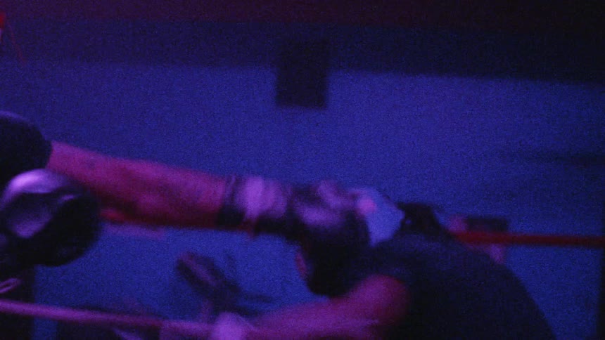Two men fight in a boxing ring illuminated by flashing blue and red lights