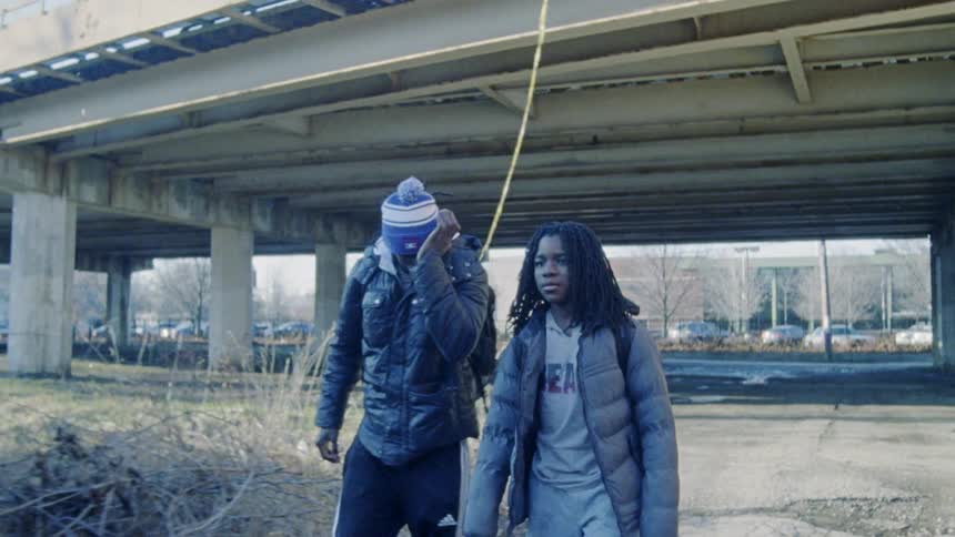 Two teenagers walk beneath an overpass in a city