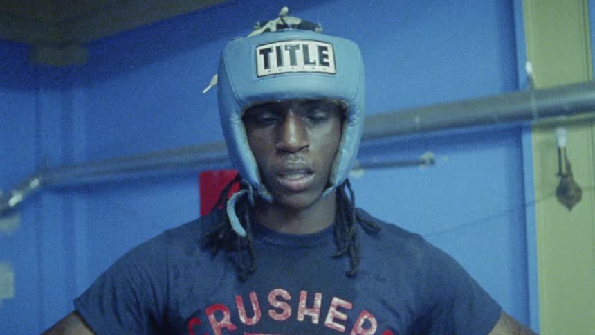 A boxer breathes heavily while leaning against the rope of a boxing ring