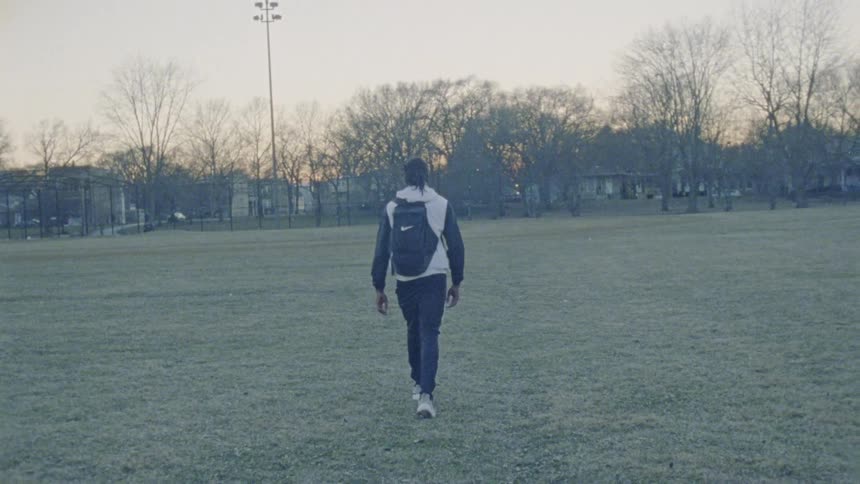 A man walks across a grass field with a backpack at sunset