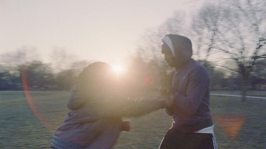 A man helps a young boy train with punches outside