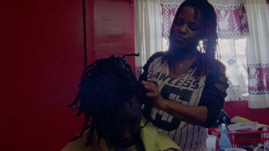 A woman in a baseball shirt cuts a young man's hair