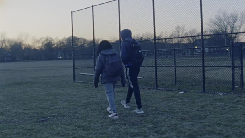 Two teenagers walk on an outdoor athletic field at sunset