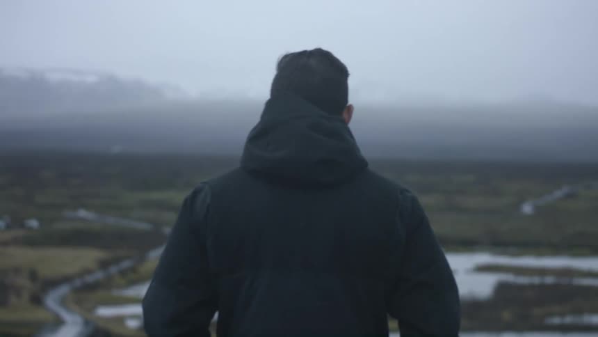 Man standing outside viewing a large field on a cloudy day