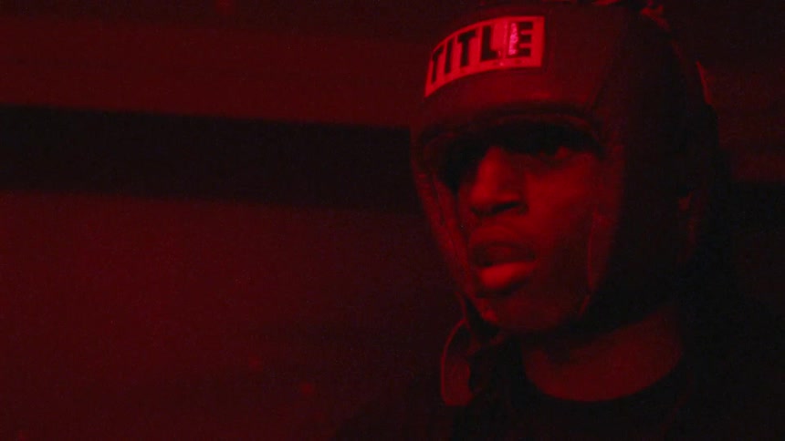 A boxer wears head protective gear in a room with flashing lights