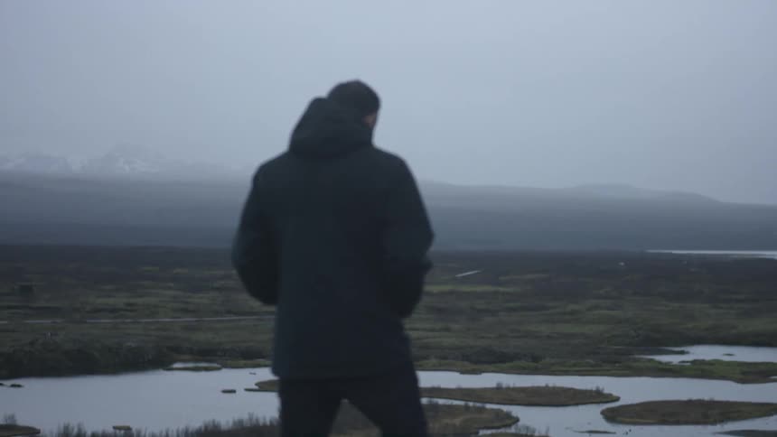 A man in a winter coat stands on a hill and looks down at wetlands