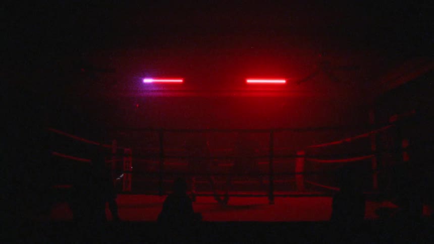 Two people fighting in a ring under flashing light