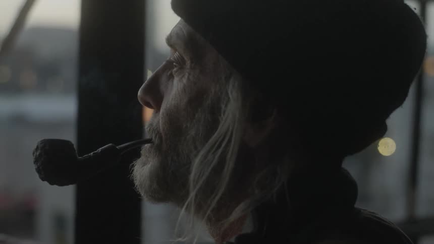 Elderly man smokes a pipe and looks out at the city