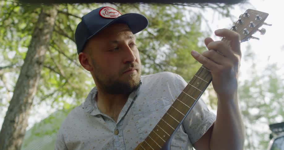 A man is playing guitar by the tree