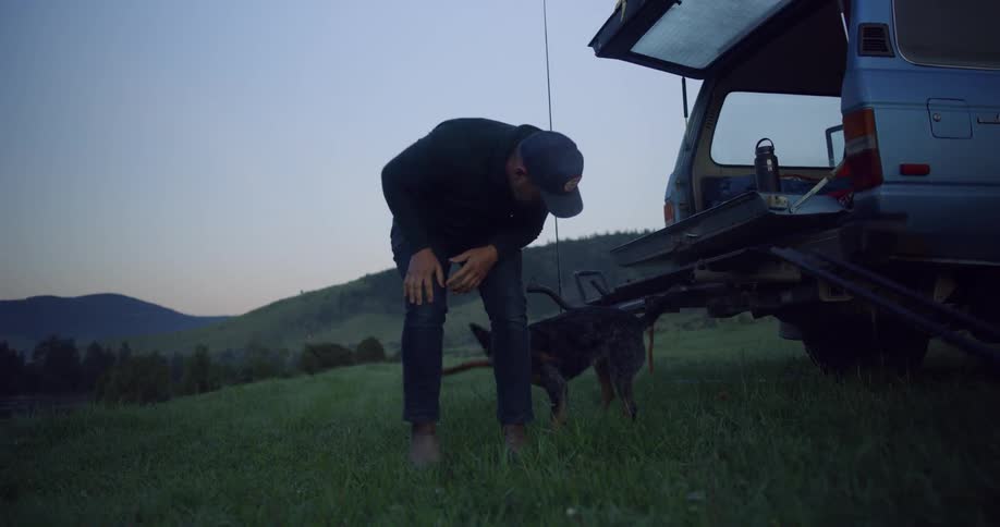 Man plays with dog on grass near car