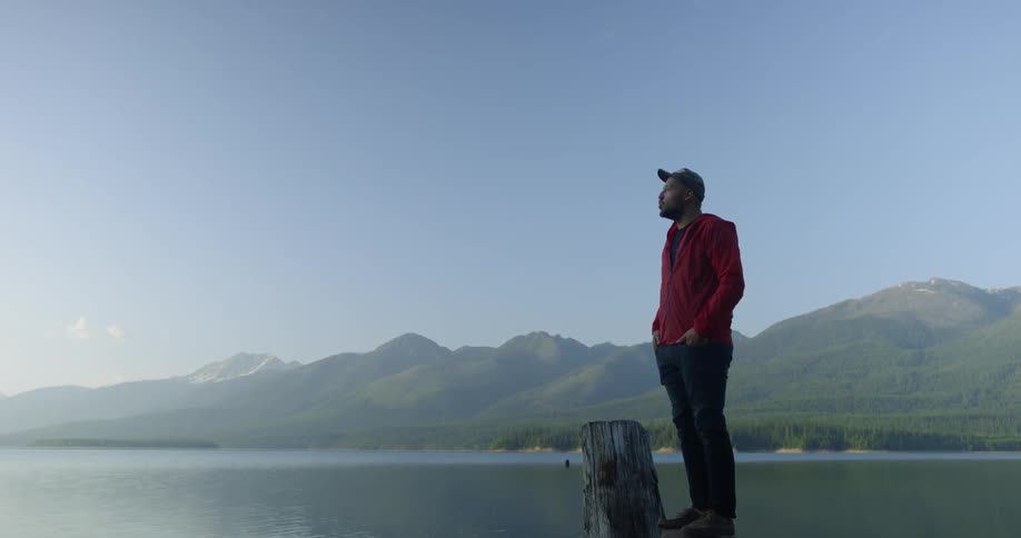 Man stands next to a backpack looking out at the lake