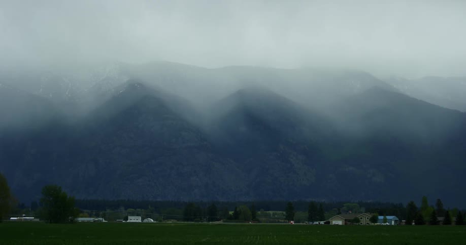 The very tall mountains are covered with fog near the homes