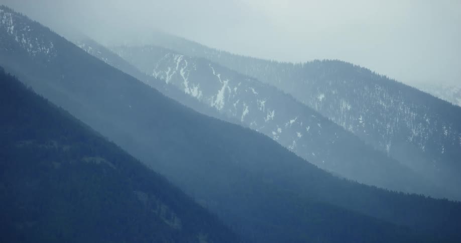 A range of mountains,  some tipped in snow, are partly occluded by cloud
