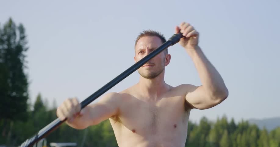 Man wearing no shirt paddles under a sunny sky