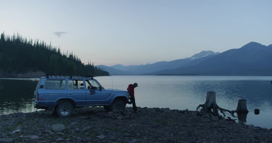 Man leans against a jeep and looks out at the lake