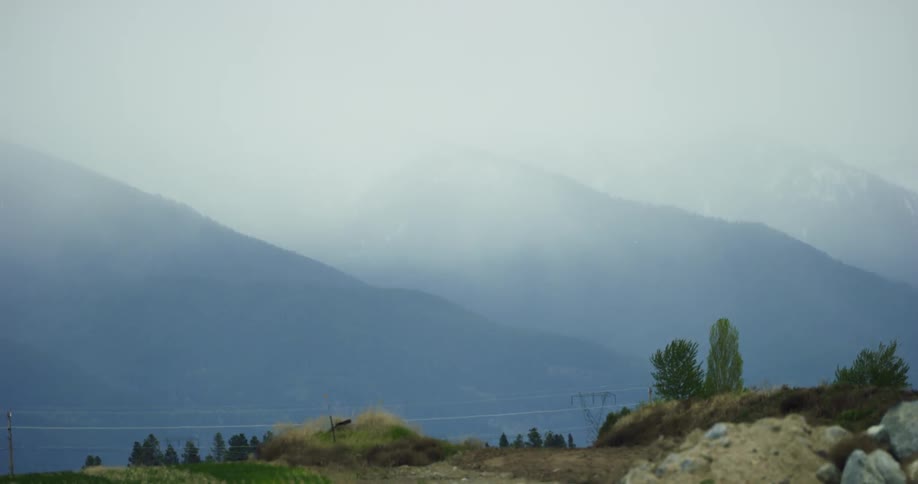 The head of the mountains are covered by clouds and the trees near the valley sway in the wind