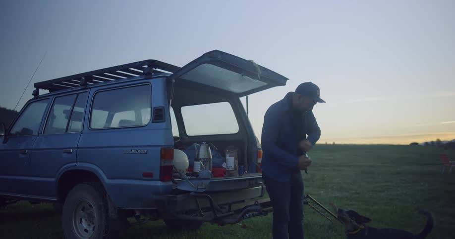 Man dog and vehicle are in the center of the meadow  doing what men dogs and vehicles dobbin the center of the meadow
