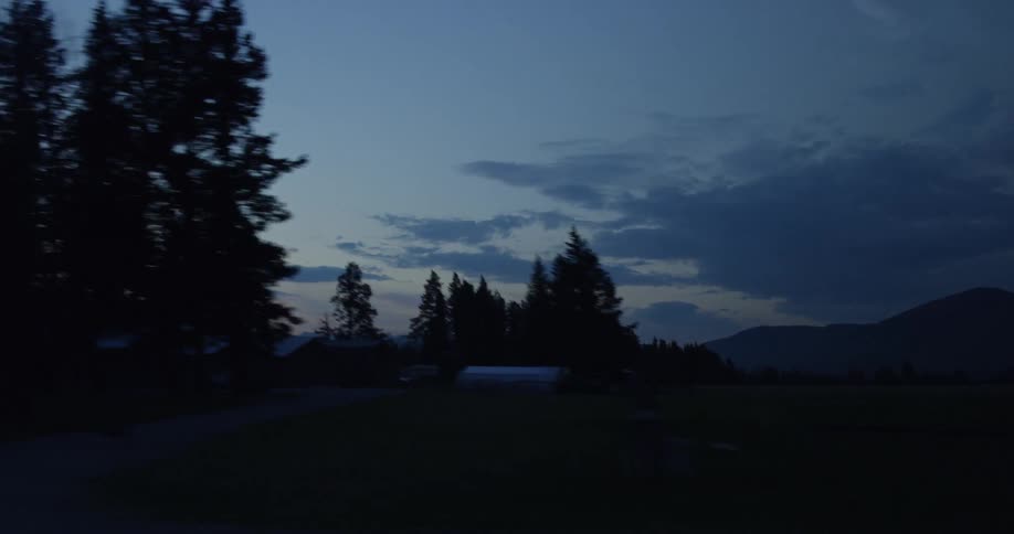 A car drives along a dark road as trees go by during sunrise