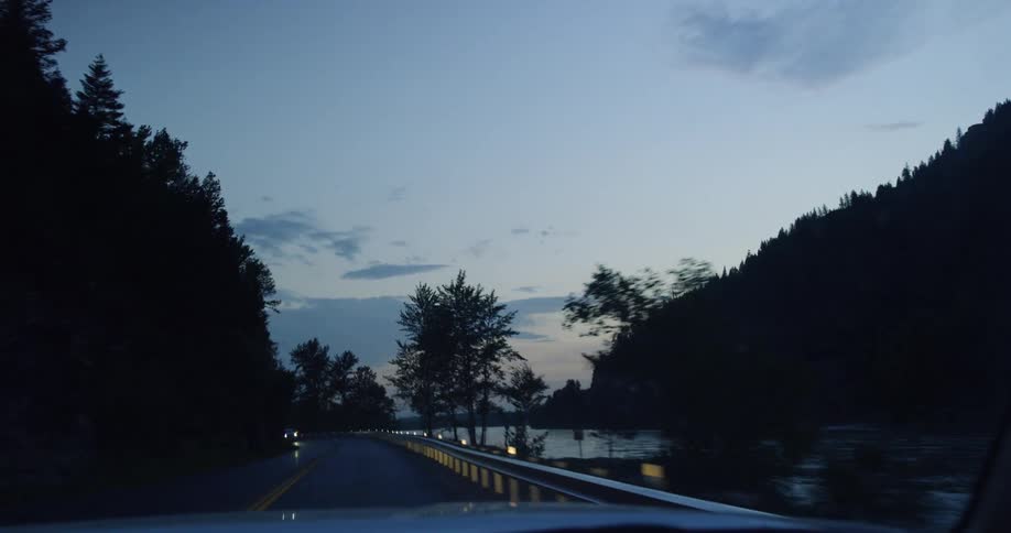 A car drives next to a river in mountains at sunset