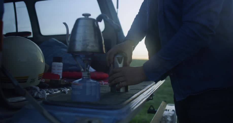 Person pouring hot water from a kettle into a coffee cup in the back of a truck