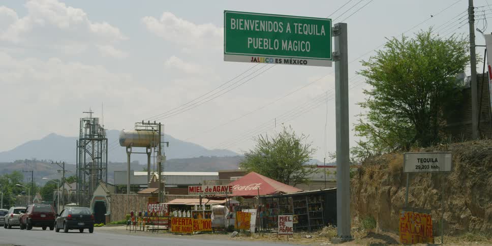 Cars drive under a sign in spanish (Welcome to Tequila, A Magical Town)