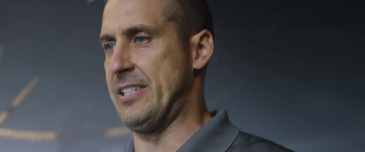 A man with a receding hairline looking down and speaking to someone before he turns and walks away