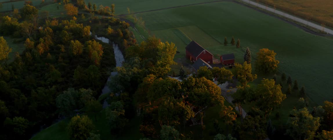 A river flows by a red barn on a rural farm at sunset