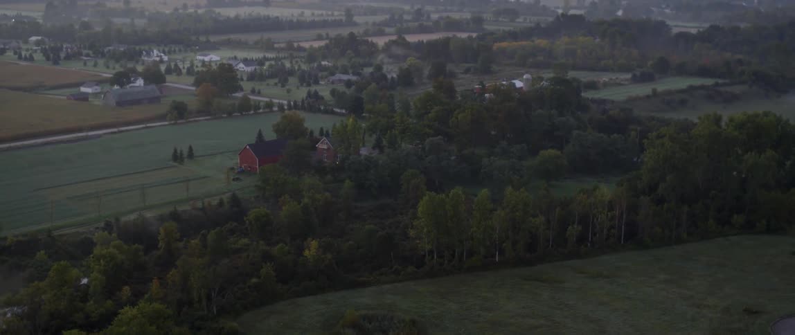 Barns and farms separated by trees all the way to the horizon at sunset