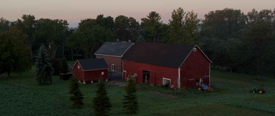 A red barn is surrounded by trees at sunset