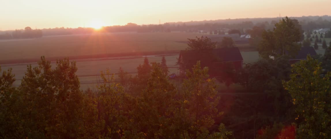 Past the forest is a large farm at sunset