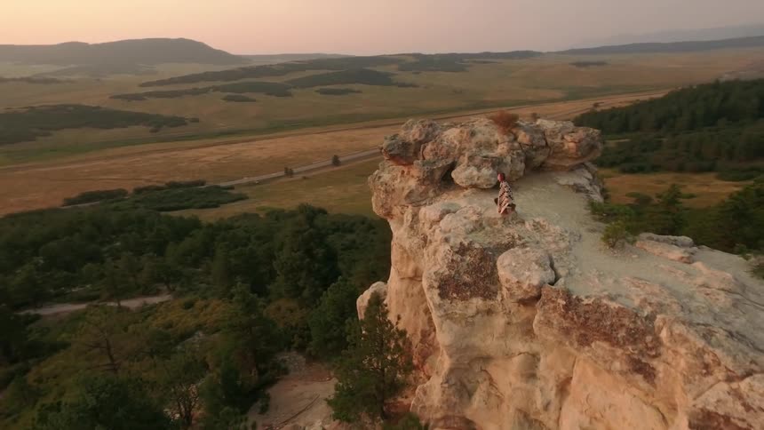 A woman standing on the edge of a cliff and overlooking a valley