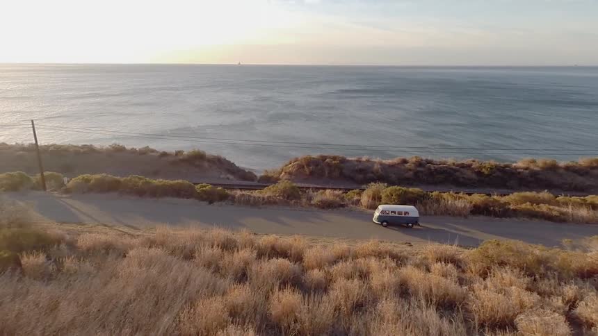 A van driving down a coastal road with the sun shining on the ocean