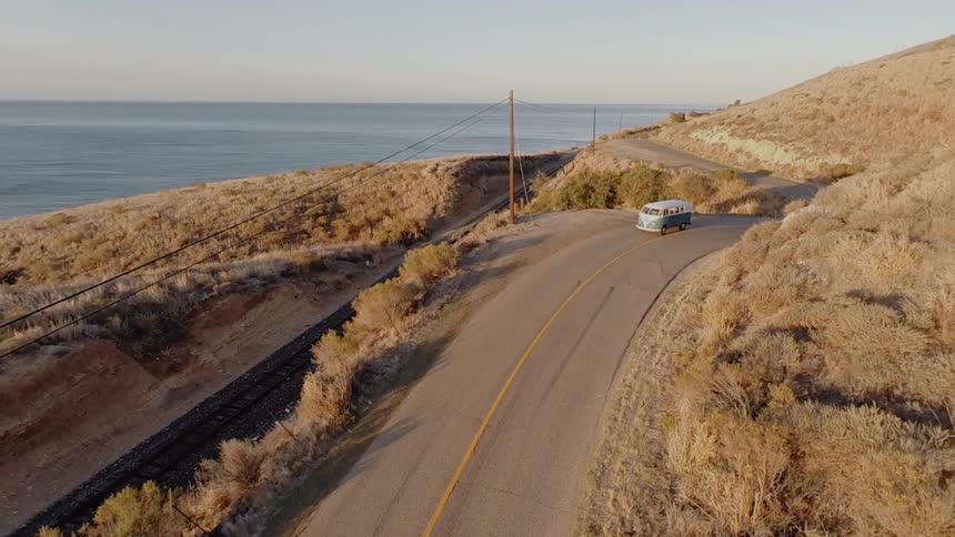 A van travels alone down a coastal highway on a sunny day