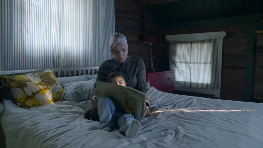 Woman and young child sit on a bed as they look at a book