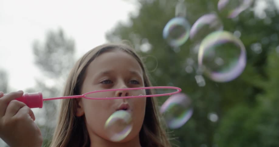 A girl smiles while blowing bubbles outside