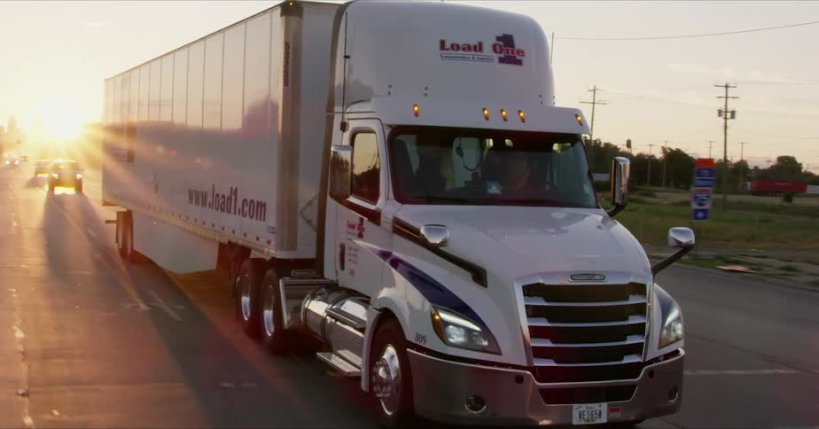 A semi truck drives on a street at sunset