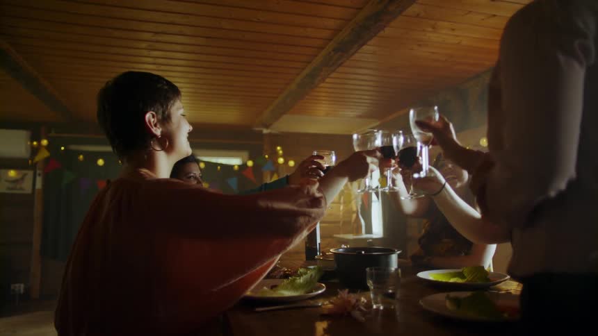 A person holds their wine glass and stands up at the head of the table