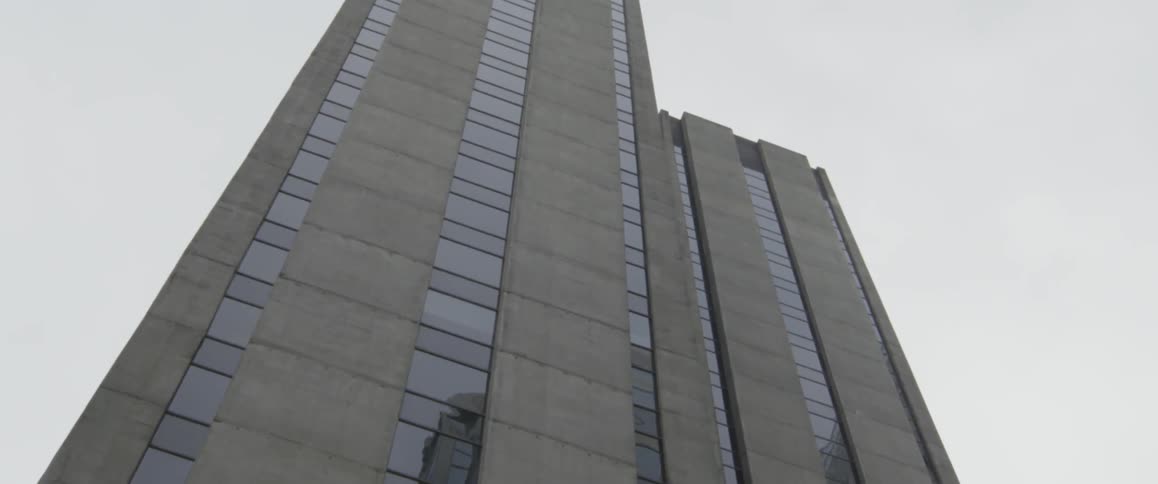 A tall building made out of concrete and glass reaches into the sky