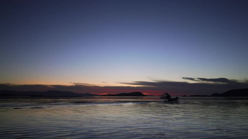 A boat floats on a lake at sunset